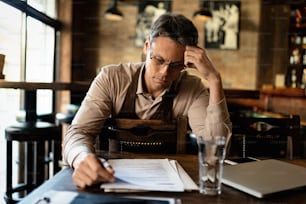 Mid adult waiter going through inventory list while doing paperwork in a pub.