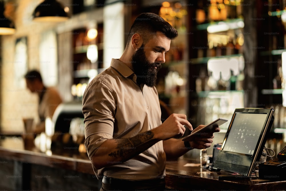 Young bartender using digital tablet while working in a pub.