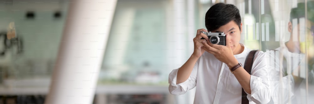 Cropped shot of young male photographer taking photo with digital camera while standing in glass wall office