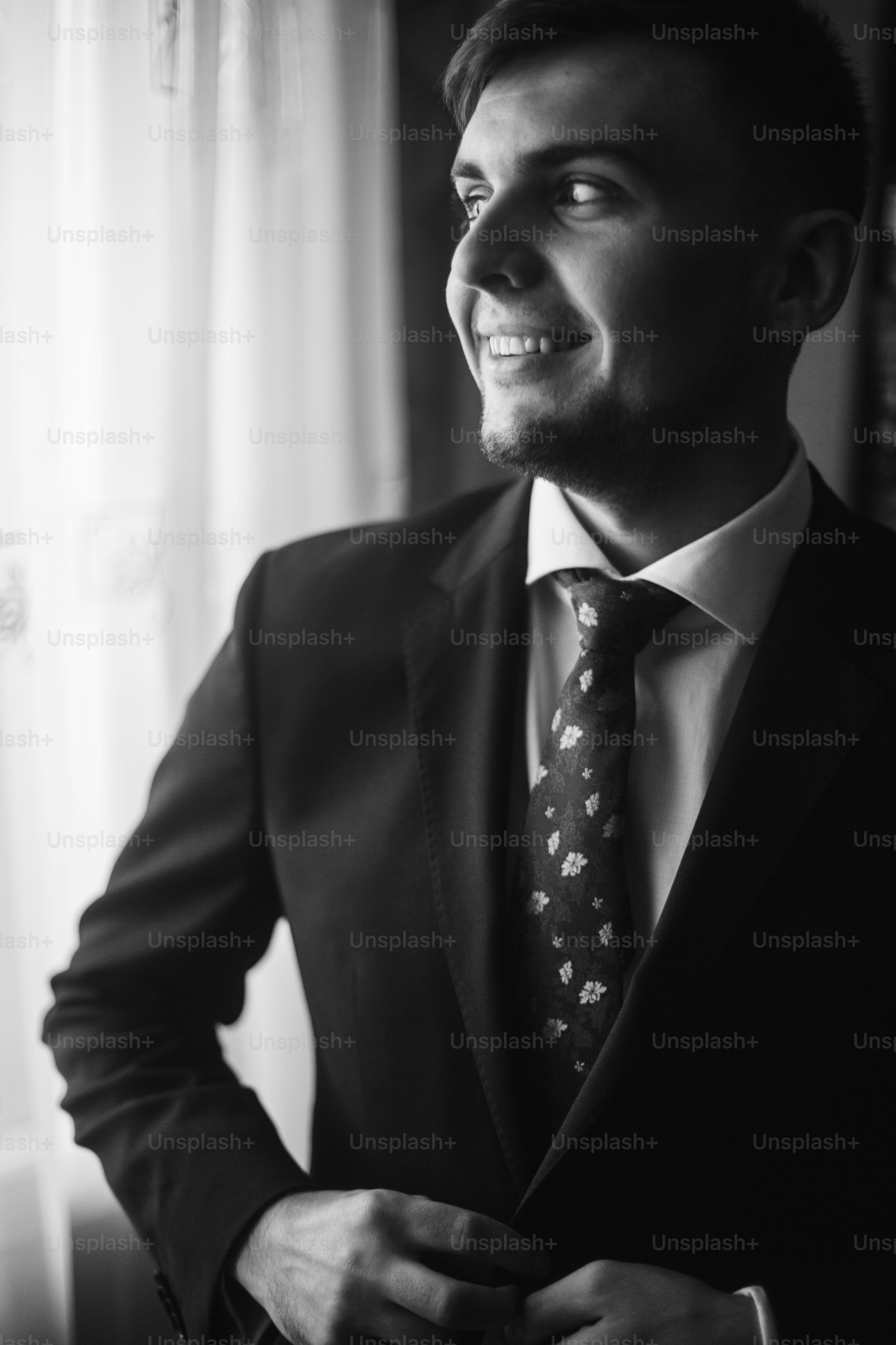 Sposo bello in camicia bianca con cravatta rossa che abbottona l'abito nero, la preparazione di nozze di mattina, uomo d'affari in giacca e cravatta che guarda fuori dalla finestra