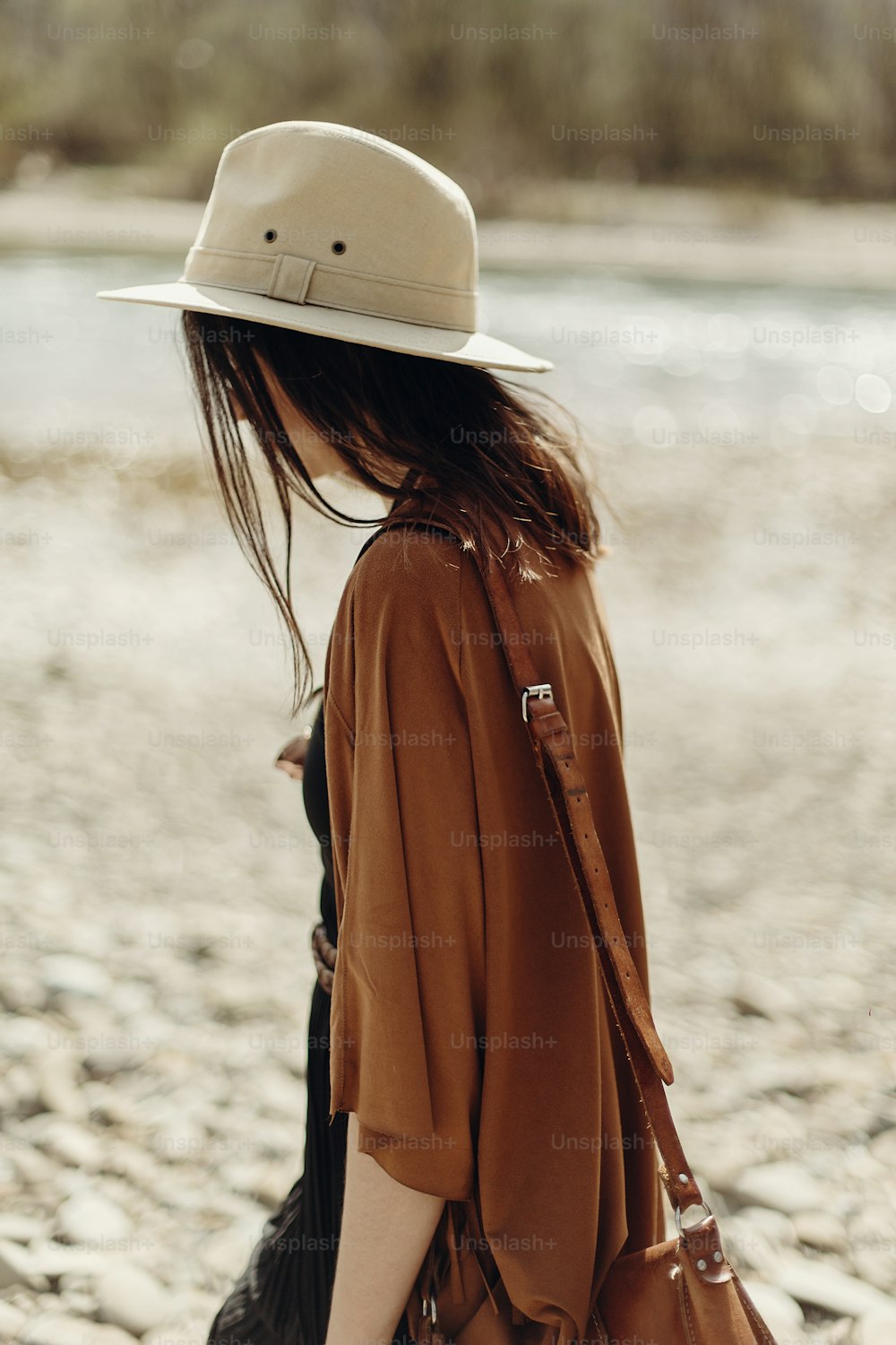 stylish hipster woman in hat, fringe poncho walking on river beach. boho traveler girl in gypsy look, summer travel. atmospheric moment.  space for text.