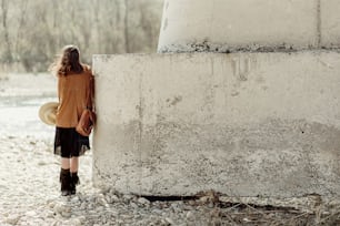 stylish boho woman posing at river under stone bridge, back view. beautiful gypsy girl with hat and fringe poncho and boots. young girl traveler. atmospheric moment. space for text