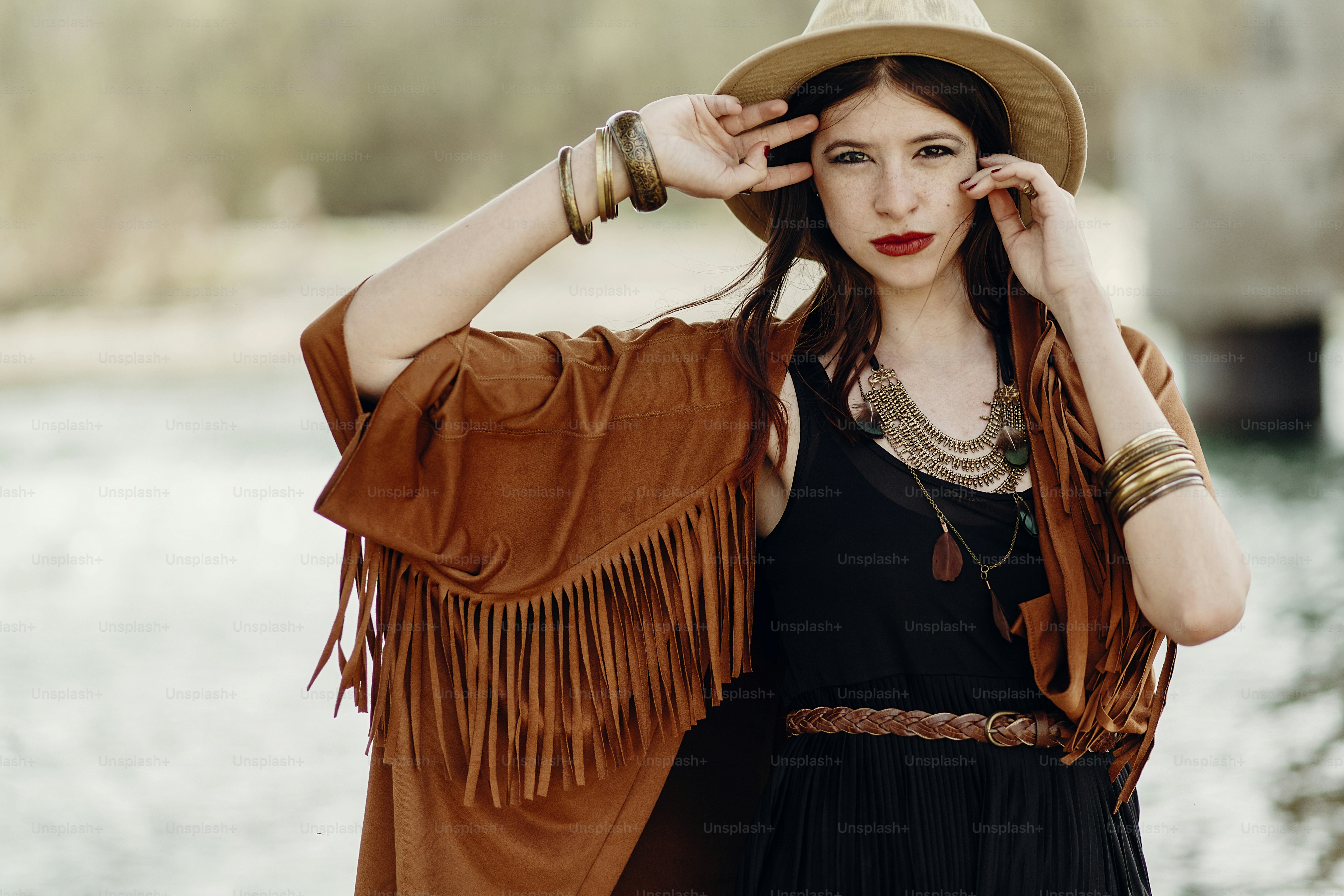 stylish hipster woman posing in hat with windy hair, in fringe poncho and accessory. boho traveler girl in gypsy look. summer travel. atmospheric moment. space for text. sensual portrait
