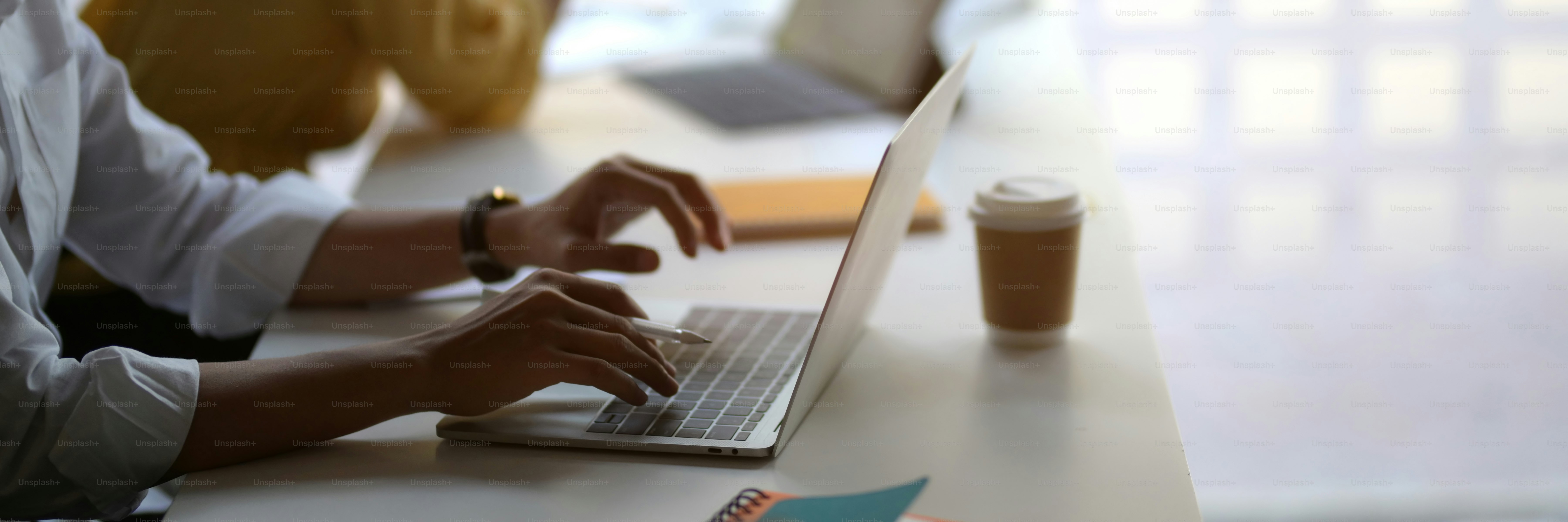 Foto recortada de hombre de negocios escribiendo en una computadora portátil con una taza de café en una mesa de madera blanca en un espacio de trabajo conjunto