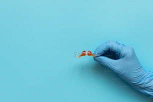 Hand of medic wearing blue latex glove holding retainer orthodontic appliance on blue background. Teeth correction concept