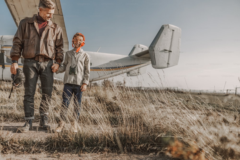Full length of smiling parent and kid holding hands with airplane on the background stock photo
