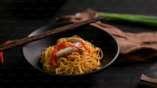 Foto cortada de Schezwan Noodles ou Chow Mein em tigela preta com pauzinhos na mesa preta