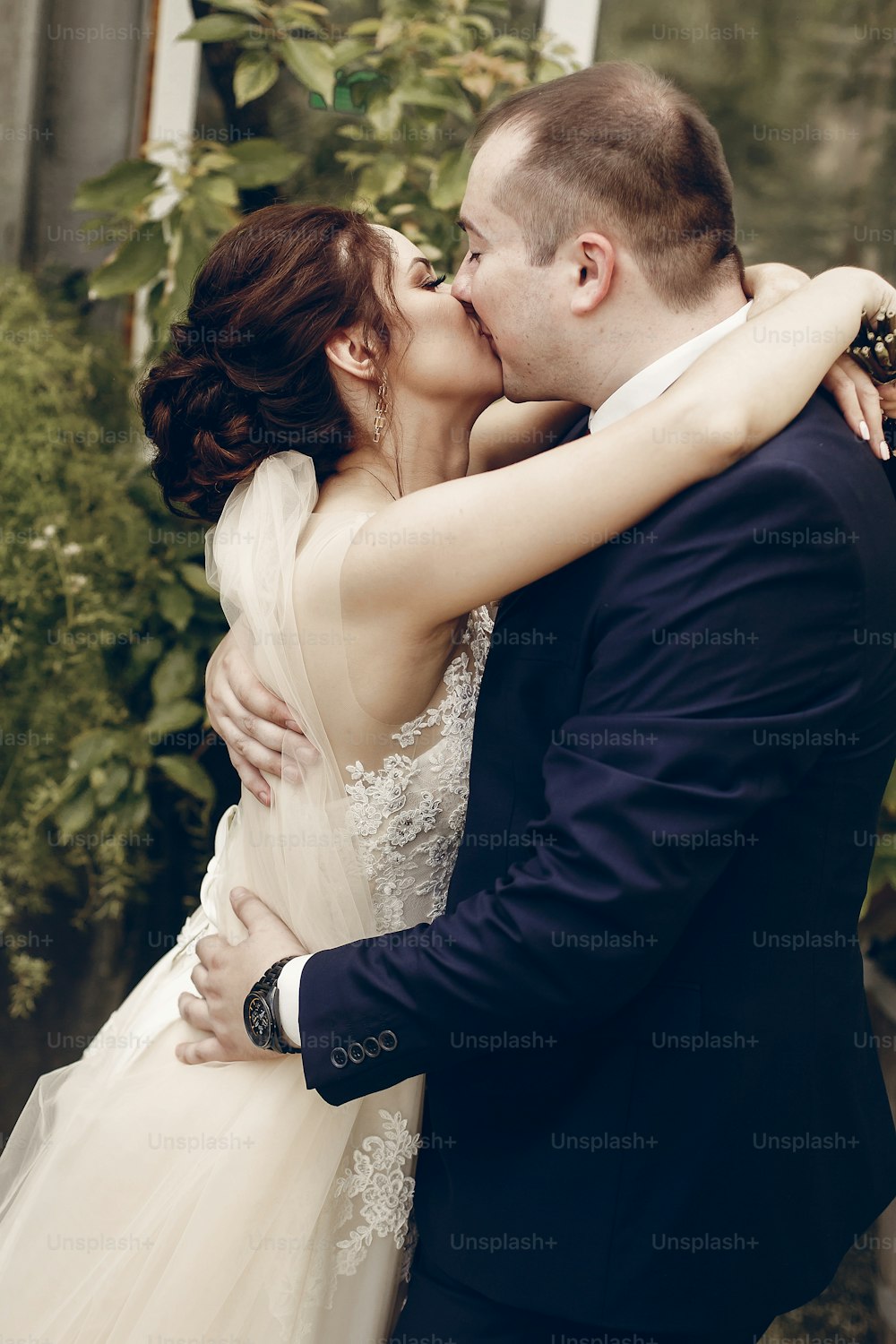 Happy newlywed couple kissing outdoors after ceremony, handsome groom embracing brunette bride in a park, newlyweds family portrait