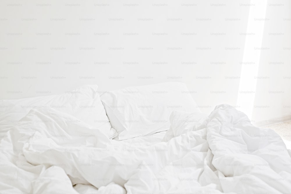 Gemütliches weißes Bett am Morgen. Weiße Bettwäsche und Kissen auf dem Bett im modernen weißen Zimmer. Faule Tage. Bleib zu Hause. Komfortabler Ort. Entspannen Sie sich am Wochenende im Hotelzimmer. Unordentliches Bett