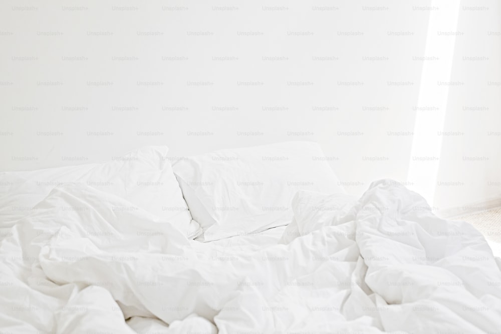 Cozy white bed in the morning. White sheets and pillow on bed in modern white room. Lazy days. Stay home. Comfortable place. Relax on weekend in hotel room. Messy bed