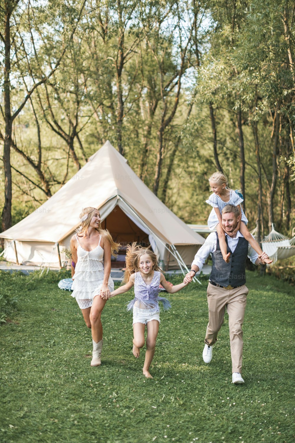 Happy Caucasian family, father mother and two little daughters, having fun outdoors in park or camping, enjoying time and laughing together, holding hands and running. Love and parenthood concept.