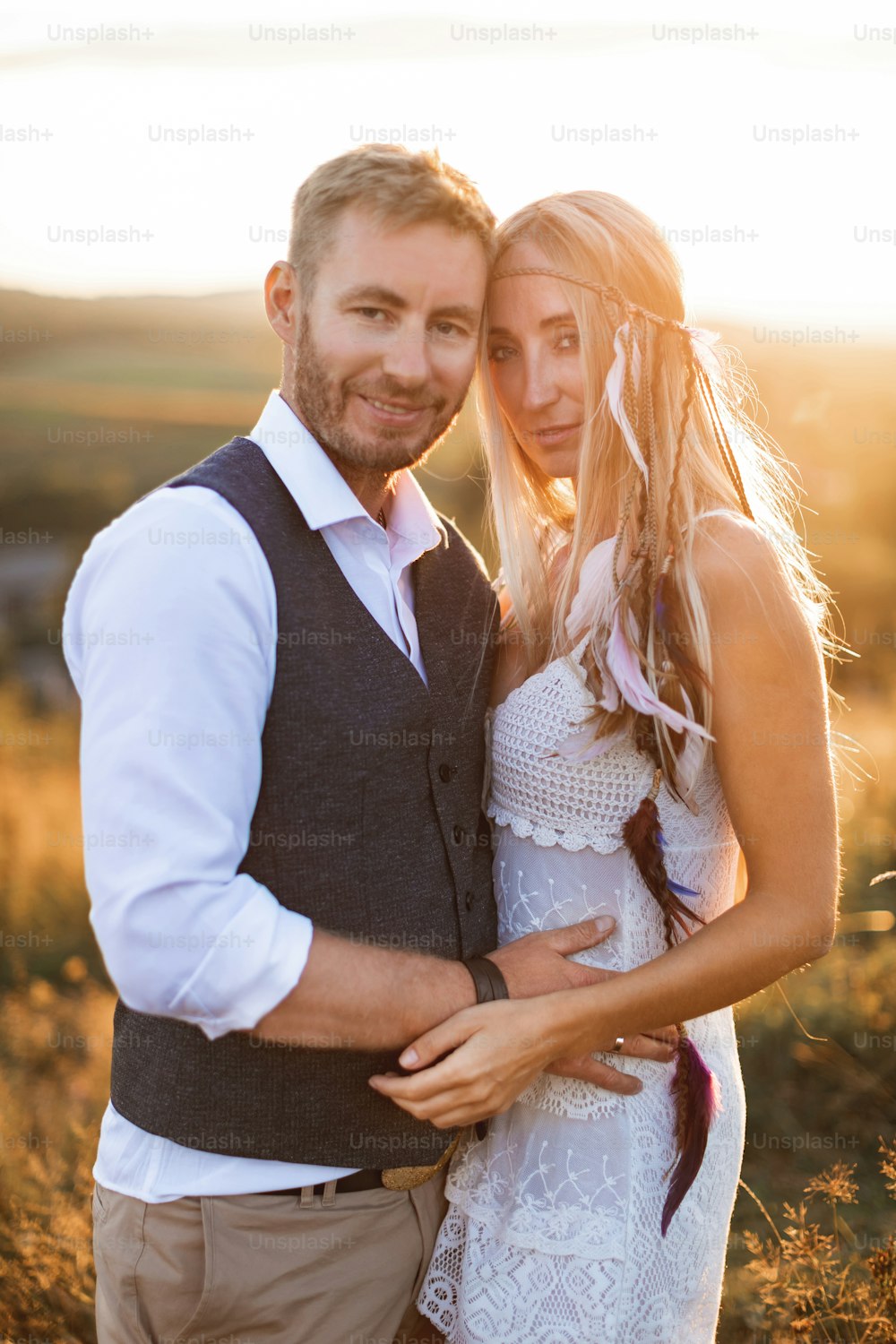 Rustic wedding and love story concept. Boho woman and man posing in summer field, hugging and looking at camera.