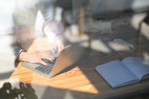 木製の作業机に一緒に座りながら、コンピューターのラップトップで作業しているビジネス開発チームの窓越しにトリミングされた画像。