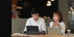 Photo of graphic designer team working together with computer laptop and tablet while sitting at the wooden working table over the modern restaurant as background.