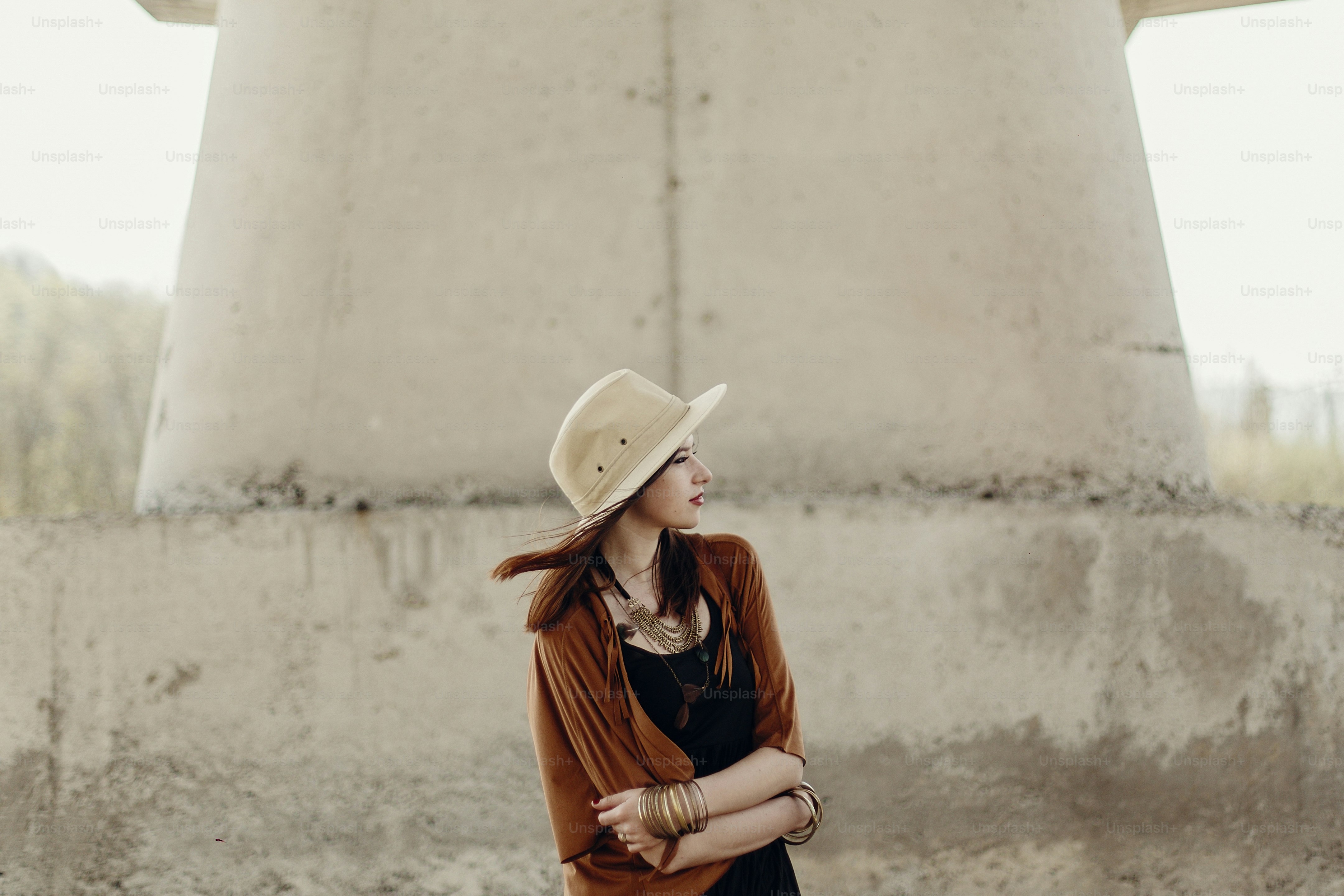 stylish hipster woman in hat with windy hair posing near river stones. boho traveler girl in gypsy look. summer travel. atmospheric moment. space for text.
