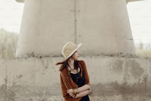 stylish hipster woman in hat with windy hair posing near river stones. boho traveler girl in gypsy look. summer travel. atmospheric moment. space for text.