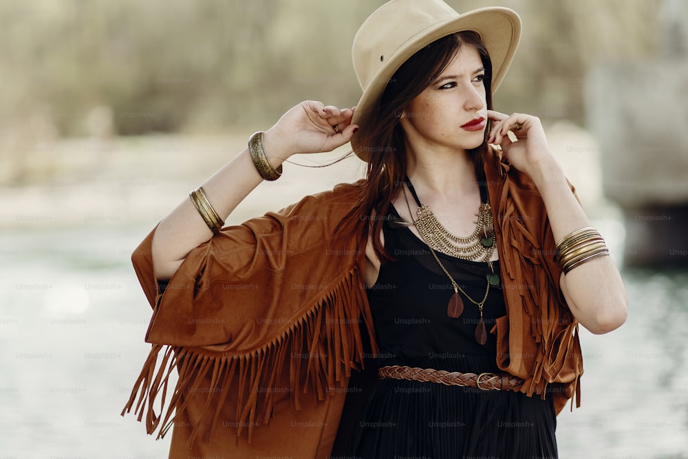 stylish hipster woman posing in hat with windy hair, in fringe poncho and accessory. boho traveler girl in gypsy look. summer travel. atmospheric moment. space for text. sensual portrait