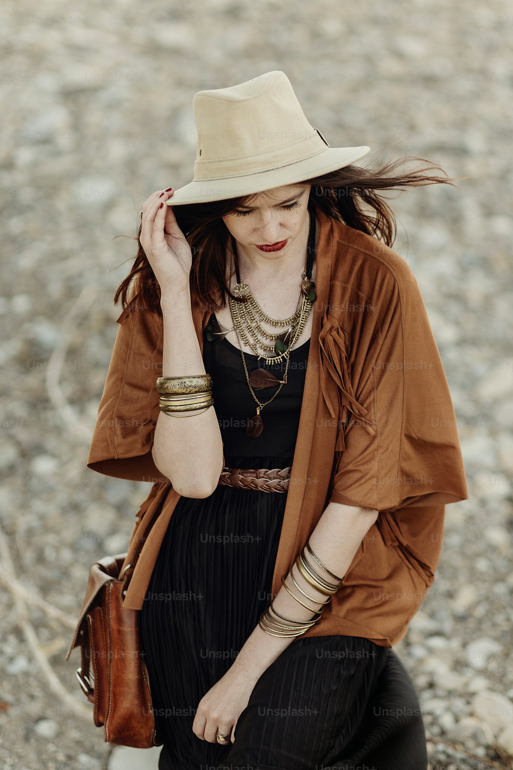 beautiful stylish boho woman with hat, fringe poncho. hipster girl in gypsy look young traveler posing near river beach in mountains. sensual look. atmospheric moment. summer travel
