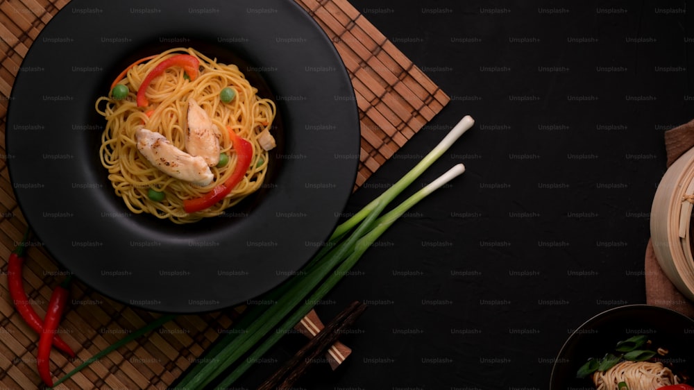 Overhead-Aufnahme von Schezwan-Nudeln oder Chow Mein mit Gemüse und Hühnchen serviert in schwarzem Teller auf schwarzem Tisch