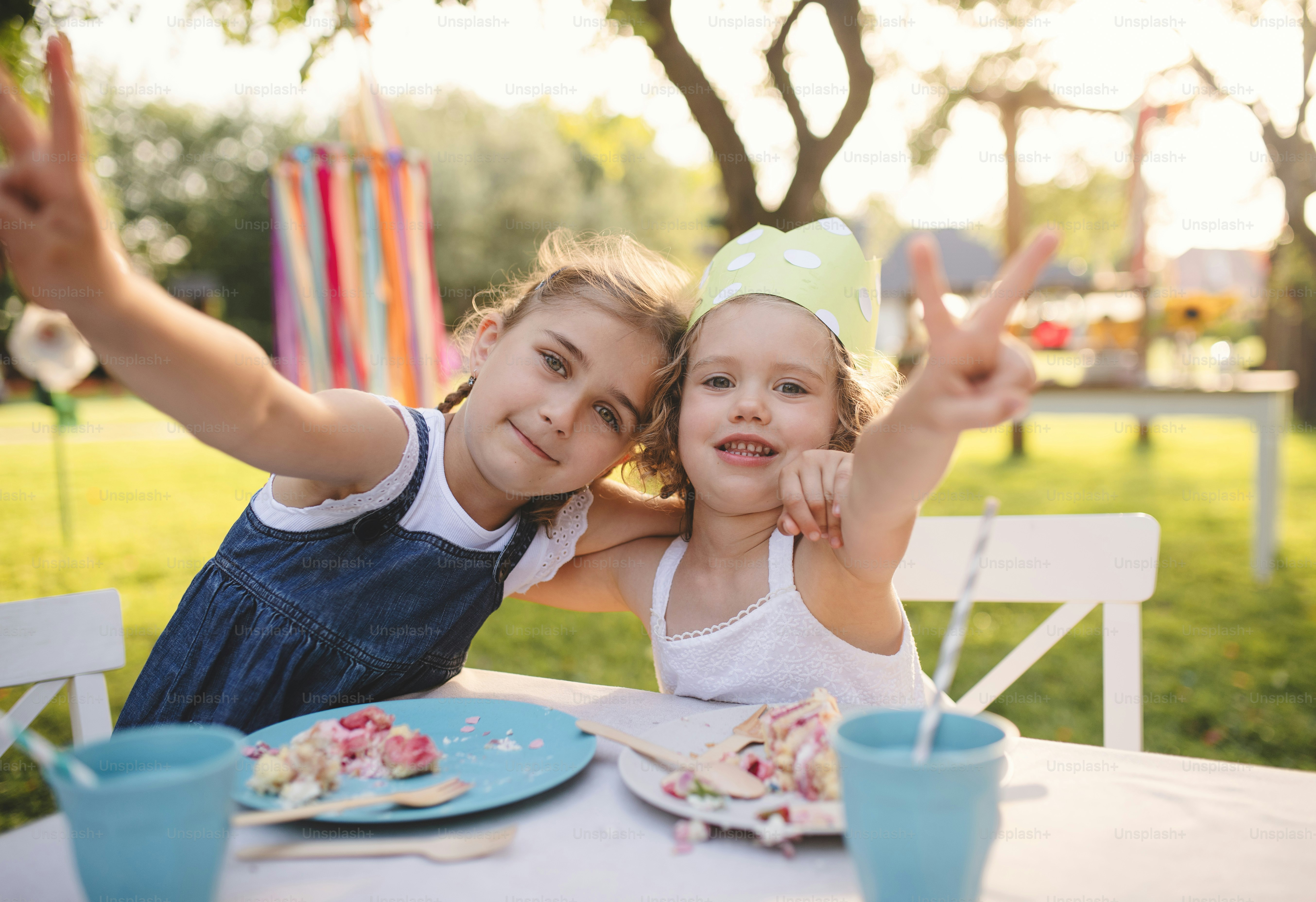 Happy small girls sitting at table on summer garden party, birthday celebration concept