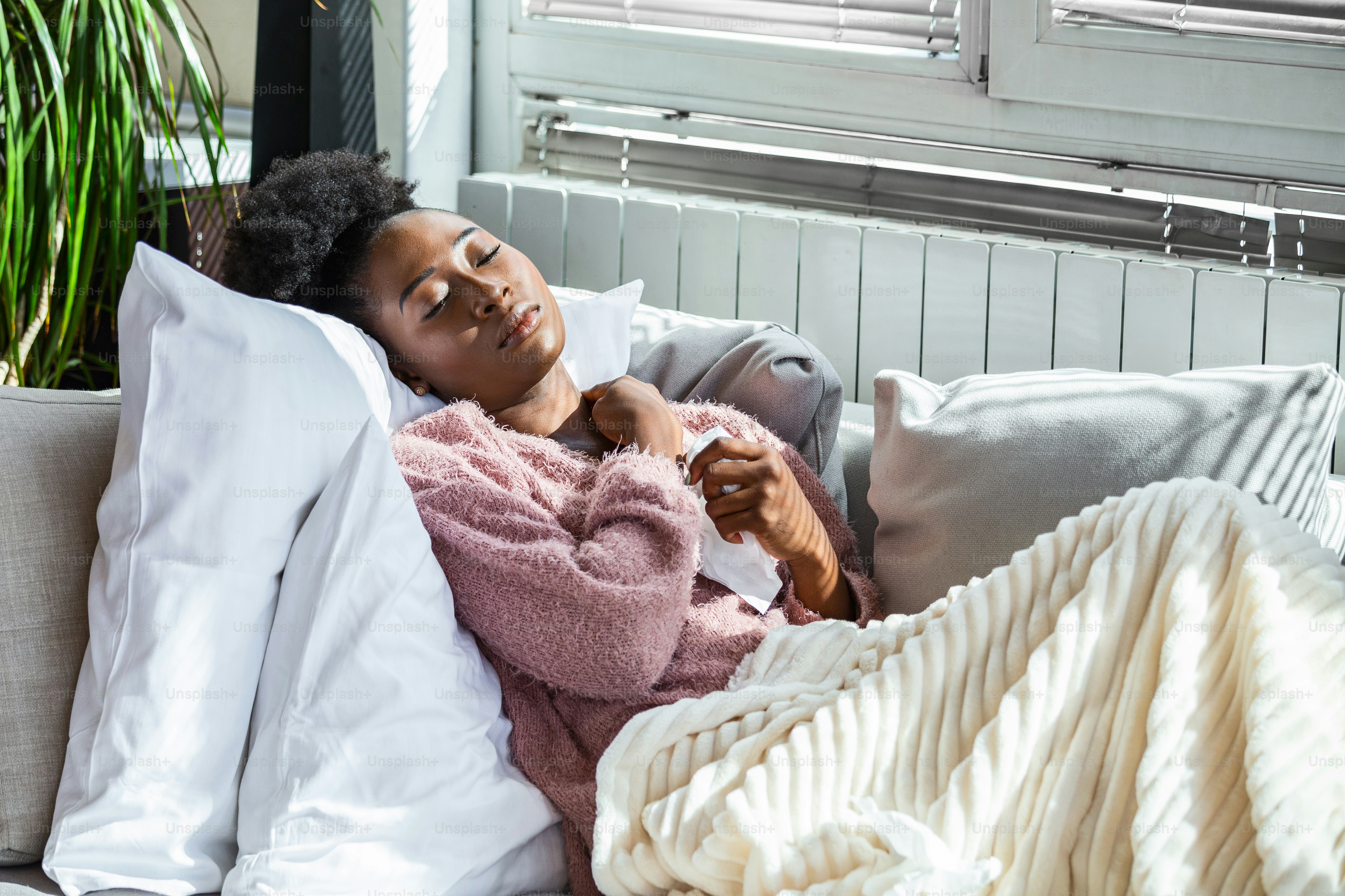 Donna malata presa dal freddo. Starnutire nei tessuti. Mal di testa. Virus. Farmaci. Giovane donna infetta dal freddo che si soffia il naso nel fazzoletto. Donna malata con mal di testa seduta su un divano