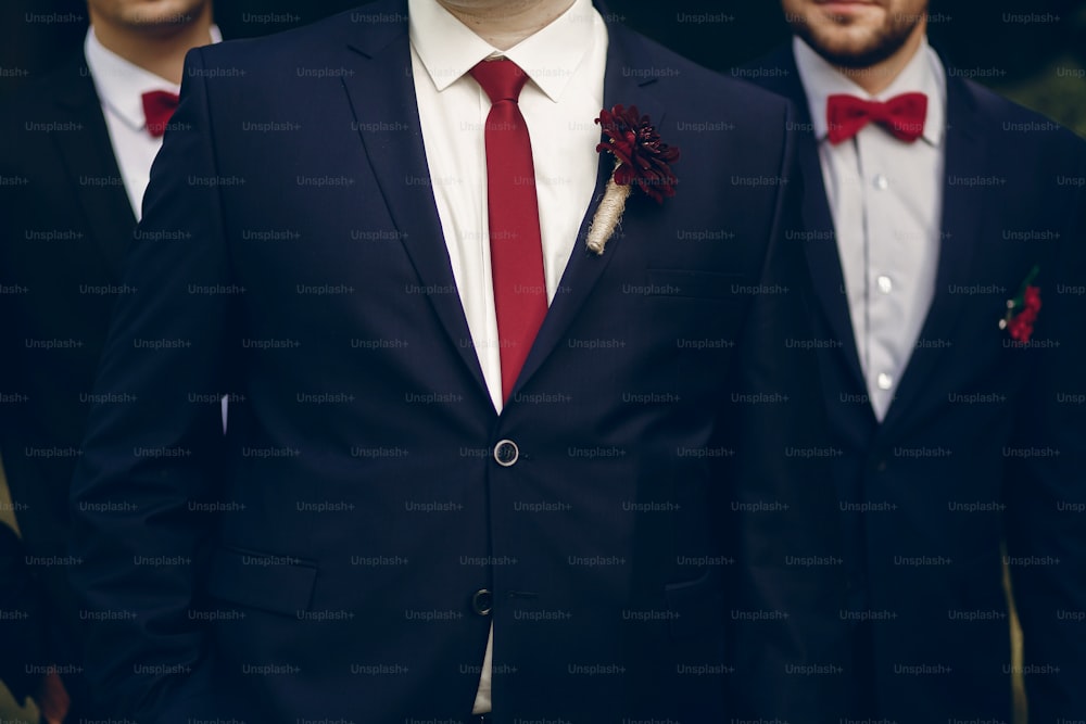 Noivo bonito e bem-sucedido posando com padrinhos ao ar livre, foto em grupo de noivos recém-casados em pé no parque com padrinhos em ternos elegantes