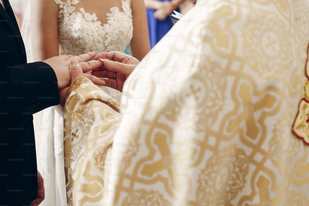 Bride and groom exchanging golden wedding rings at wedding ceremony in christian church, priest putting on wedding ring on sensual bride and groom closeup