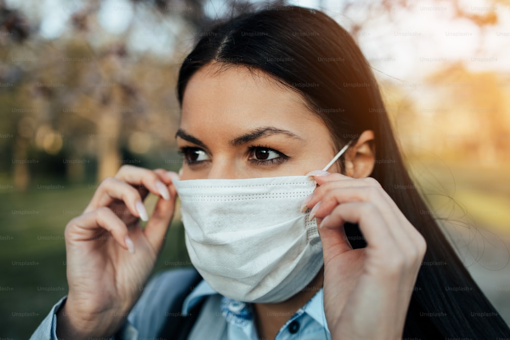 Close up shot of elegant business woman standing in city park and wearing protective mask to protect herself from dangerous flu or virus. Corona virus or Covid-19 concept.