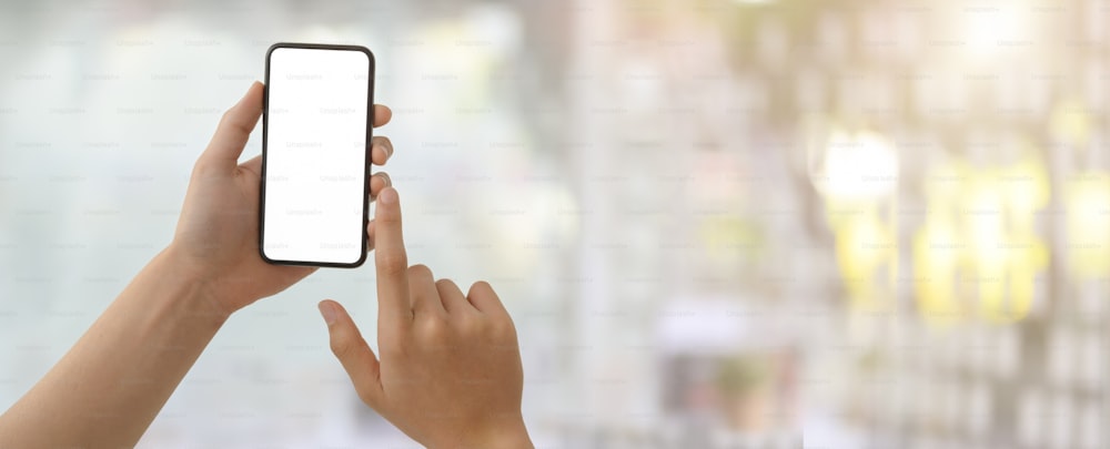 Cropped shot of a man touching on blank screen smartphone in blurred glass wall office room background