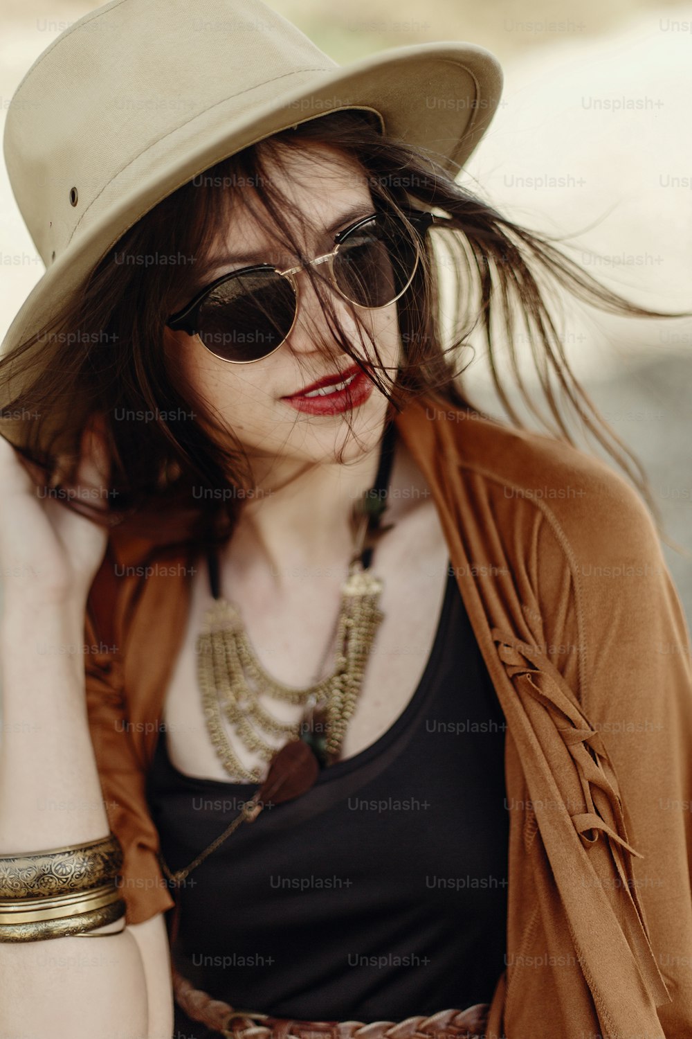 바람이 부는 머리를 가진 모자를 들고 선글라스를 쓴 아름다운 세련된 힙스터 여성. 보헤미안 여행자 소녀 집시 모습, 산의 해변 근처. 대기 순간. 여름 여행. 텍스트 공간.