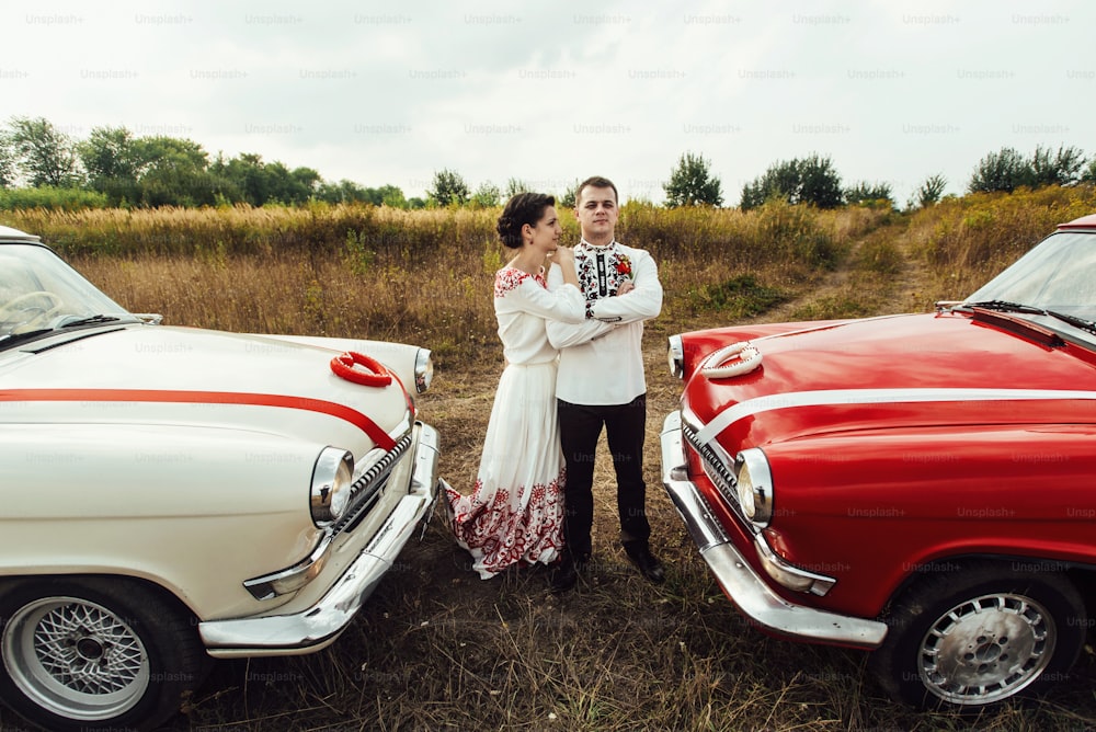 stylish bride and happy groom near  two retro cars on the background of nature