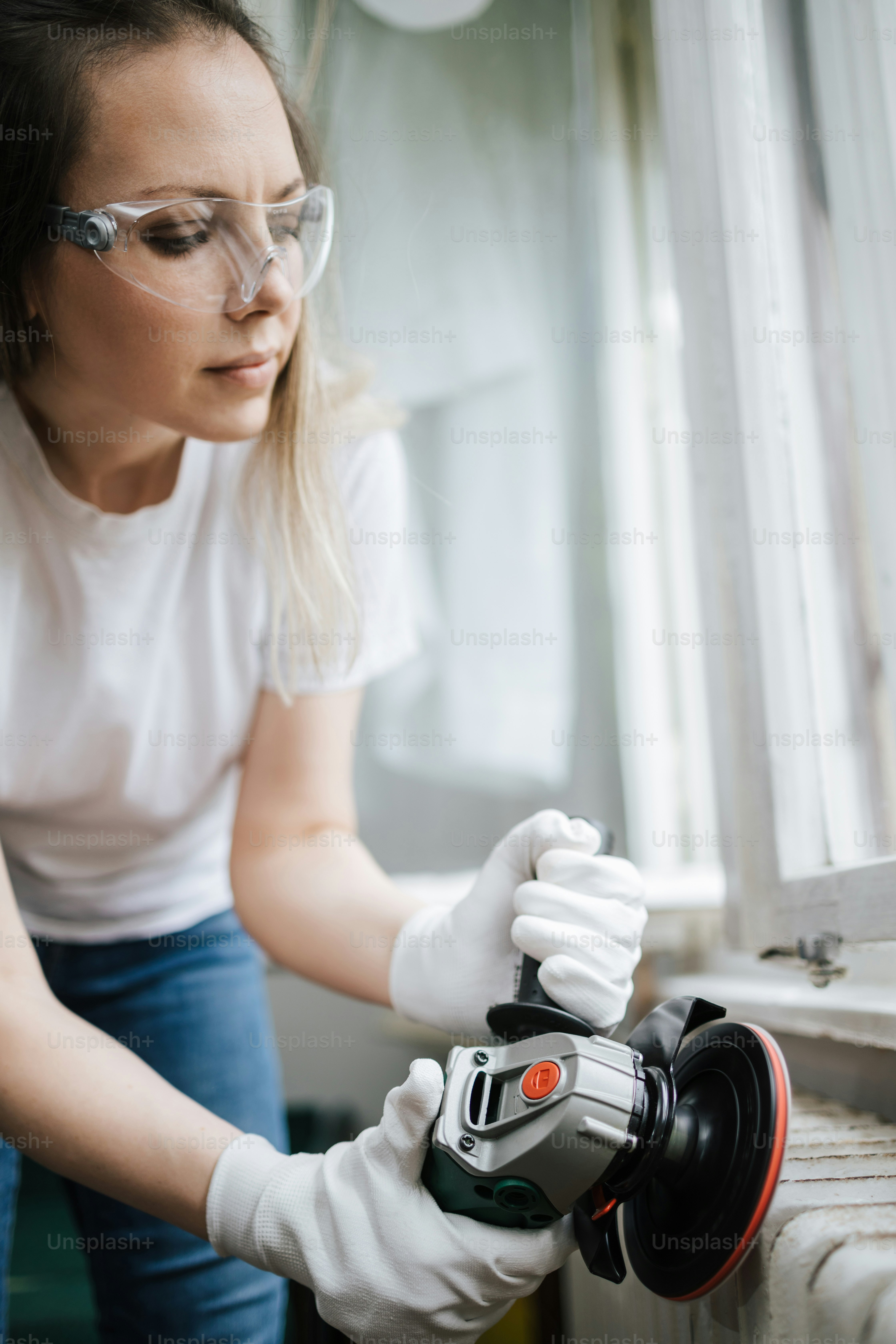 Schöne und fleißige Handwerkerin mittleren Alters, die ihr altes Haus oder ihre Wohnung renoviert. Sie hält einen professionellen Schleifer und Bürstenheizkörper für die spätere Malerei. Do-it-yourself-Hausarbeitskonzept.