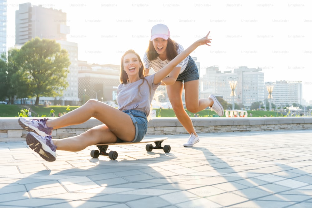 Two smiling young girls having fun while riding on a skateboard at the park
