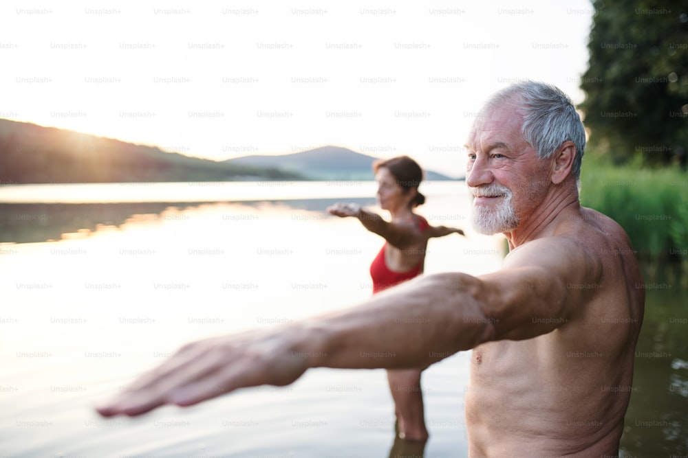 Senior couple in swimsuit standing in lake outdoors before swimming, doing exercise.