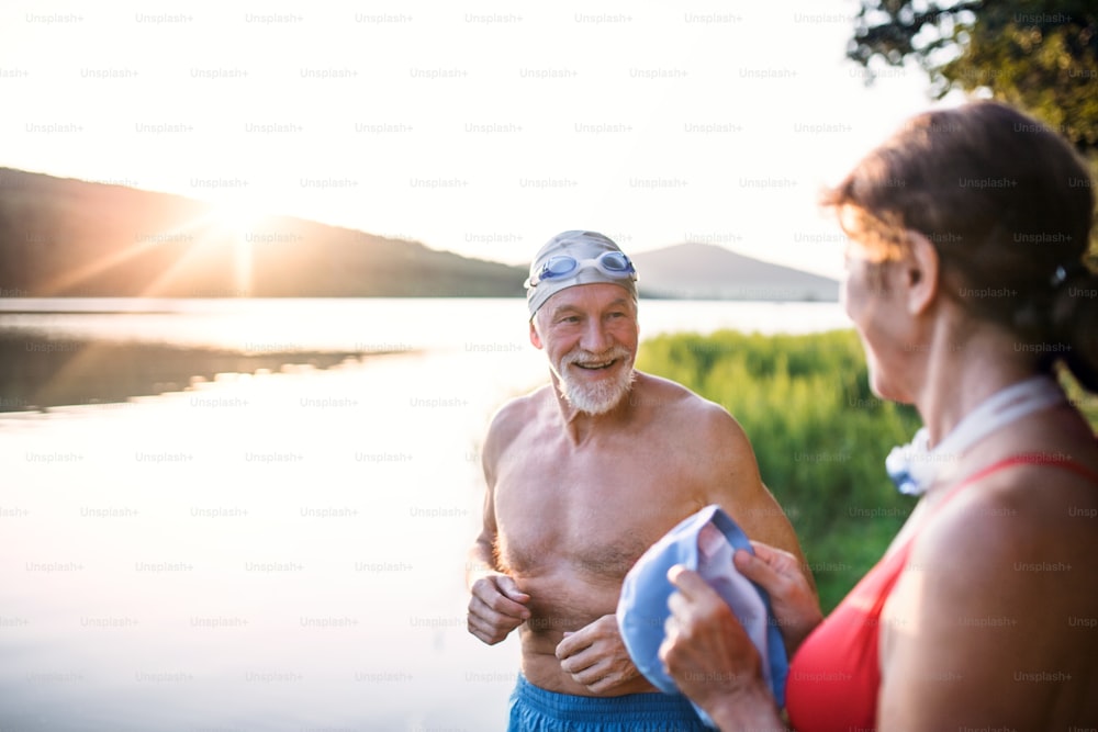 Senior couple in swimsuit standing by lake outdoors before swimming. Copy space.