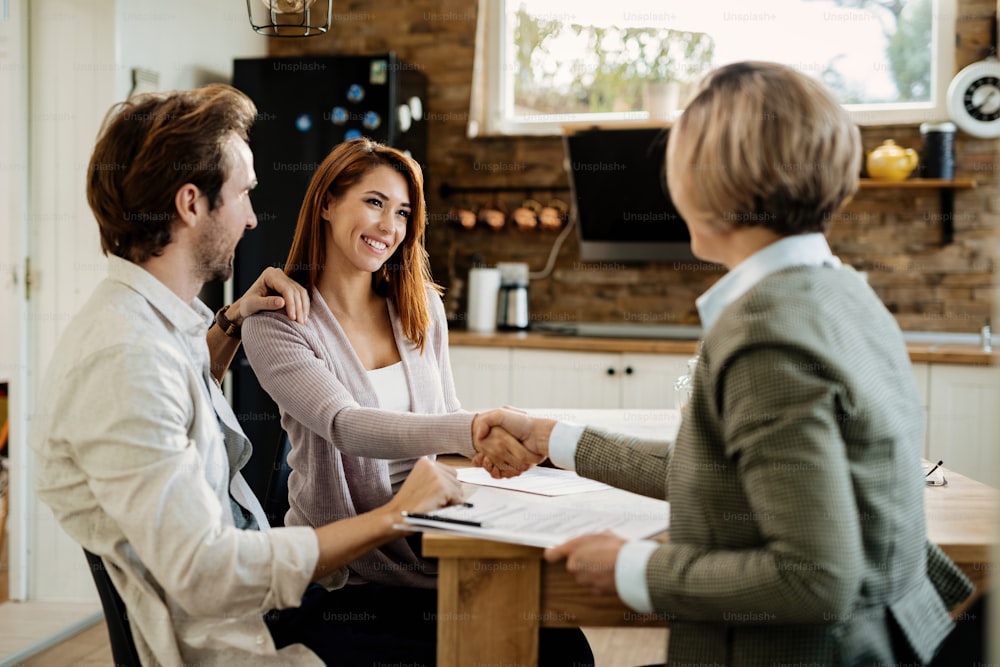 Happy couple making a deal with financial advisor on a meeting at home. Focus is on woman shaking hands with the advisor.