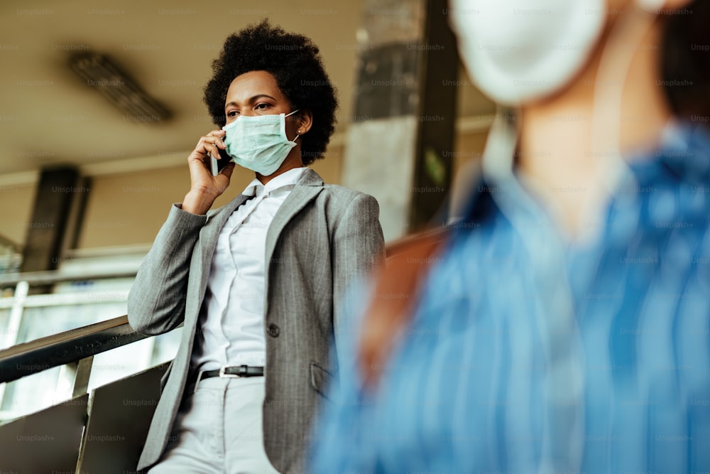 African American businesswoman wearing face mask against viruses while walking through railroad station corridor.