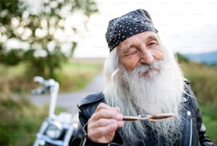 Senior man traveller with motorbike and sunglasses in countryside, winking.