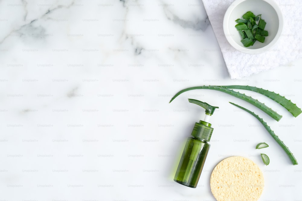 Natural organic cosmetic lotion bottle, sponge and sliced stems aloe vera on marble background. Flat lay, top view. Skin care, SPA, beauty treatment concept.