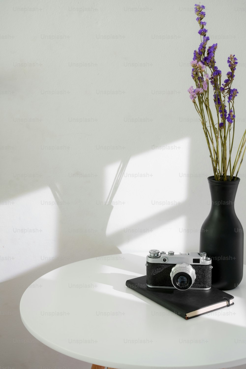 Moderne Wohneinrichtung des Wohnzimmers mit Keramikvase, Kamera und Notebook auf weißem Kreistisch mit weißer Wand