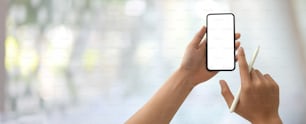 Cropped shot of a man using blank screen smartphone while holding stylus  in blurred office room background