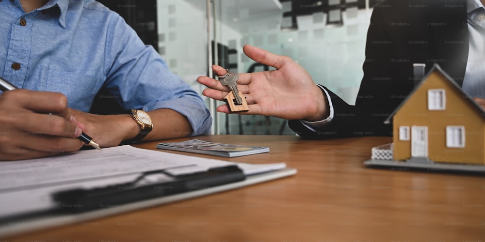 Cropped image of Real estate agent offer house insurance or house ownership to smart man in blue shirt"n at the modern wooden table. Signing on agreement, Broker/Seller/Dealer concept.