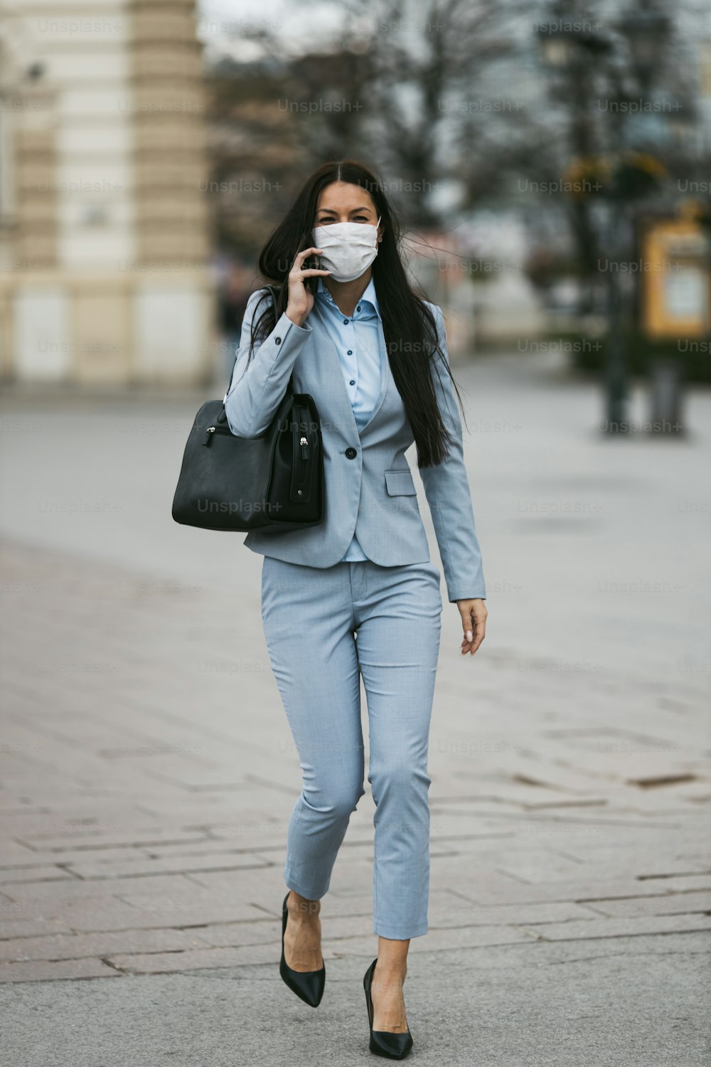 Young and elegant business woman walking on empty city street and wearing protective mask to protect herself from dangerous flu or virus. Corona virus or Covid-19 concept.