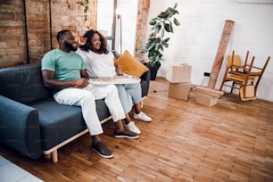 Young Afro American couple sitting on the sofa with pizza after moving into new apartment