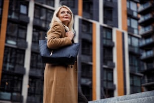 Low angle of a calm pleasant female with a handbag on her shoulder looking away