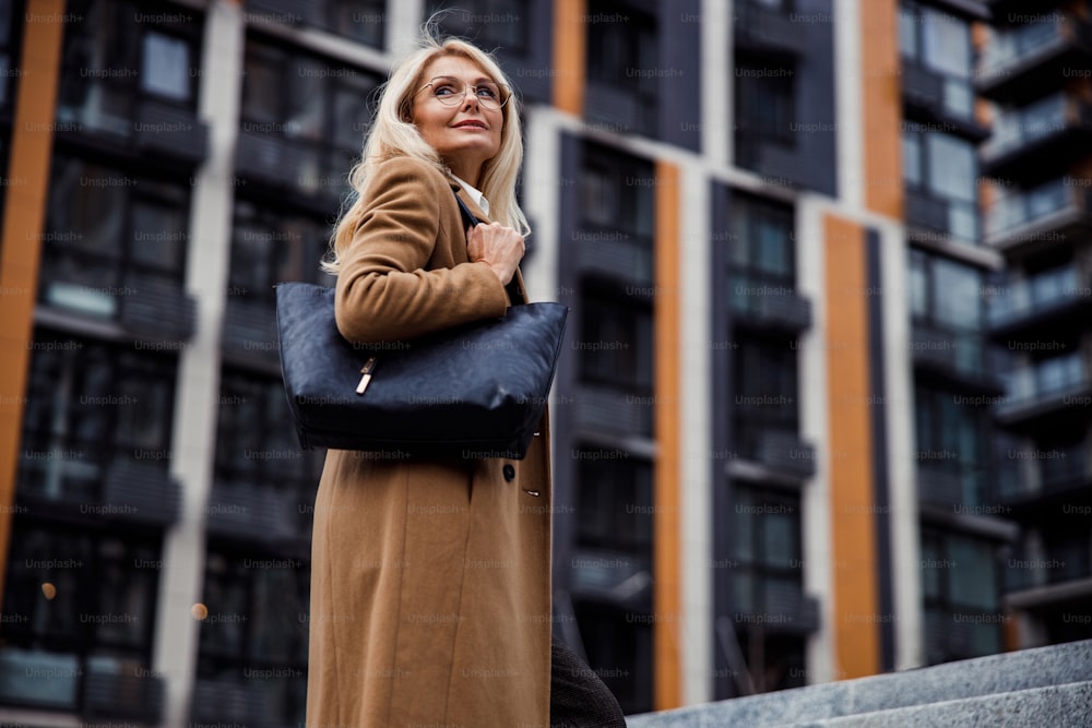 Low angle of a calm pleasant female with a handbag on her shoulder looking away