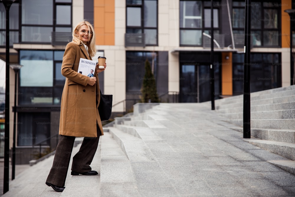 Full-sized portrait of a joyous businesswoman in a double-breasted coat looking in front of her