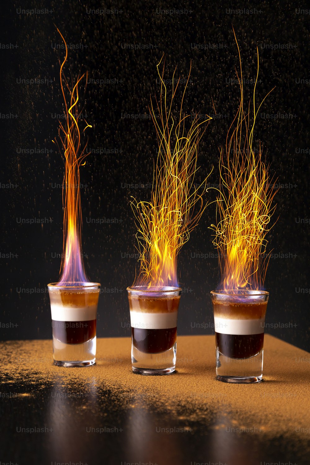 Tre bicchierini di cocktail B-52 in fiamme posti sul bancone di un bar, con una spolverata di cannella in polvere che provoca scintille
