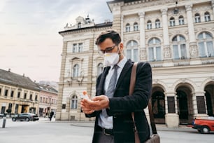 Elegante hombre de negocios con mascarilla protectora que usa alcohol en aerosol para desinfectar sus manos. Concepto de pandemia o epidemia de virus.