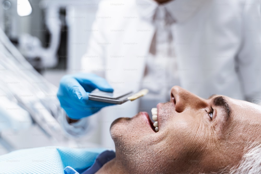Hombre alegre está acostado en el sillón dental mientras el dentista lo prepara para los procedimientos con dientes